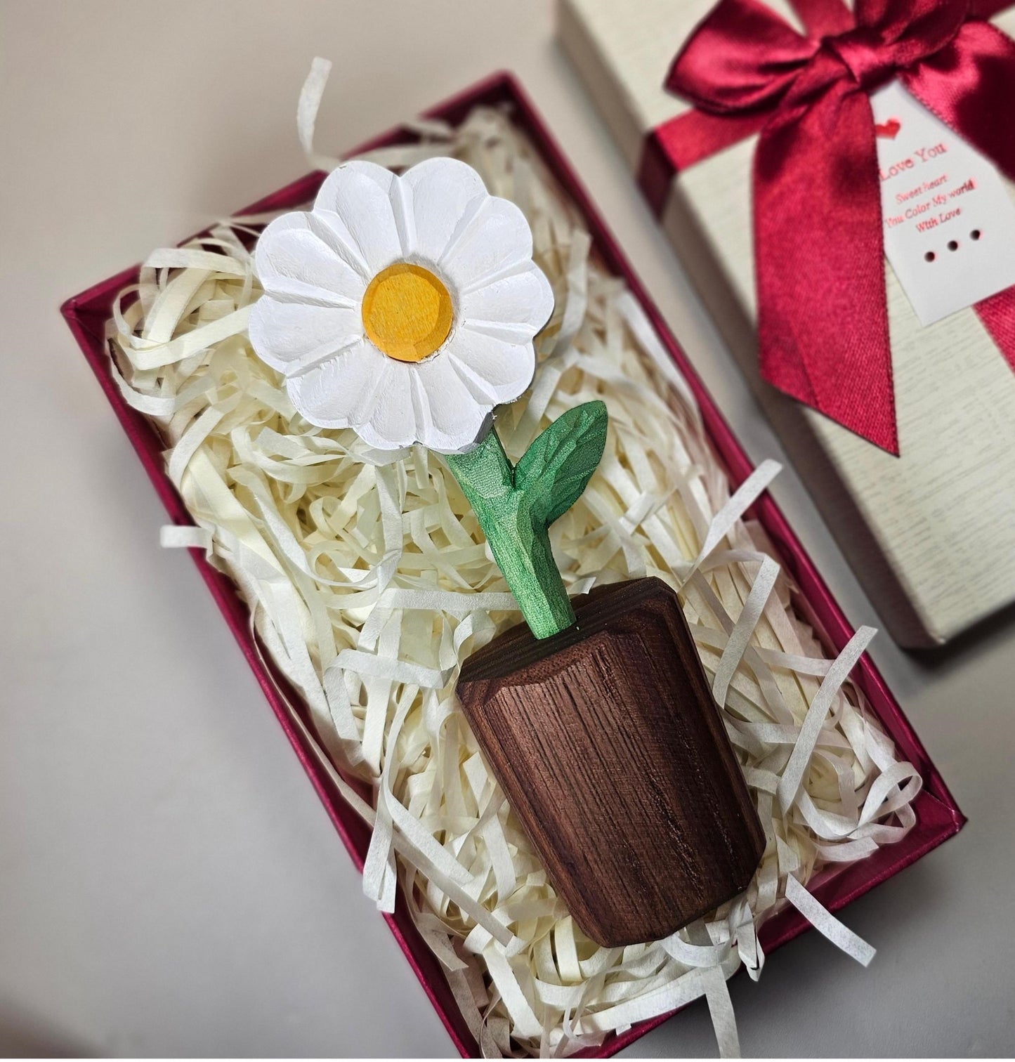 Handcrafted wooden sculpture of a daisy flower with a brown stem and green leaves, displayed on a table.