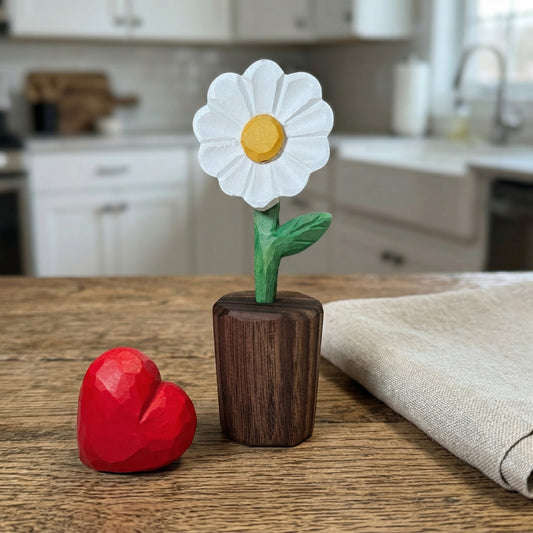 Decorative items including a white flower with a yellow center and red heart on a wooden surface in a kitchen.