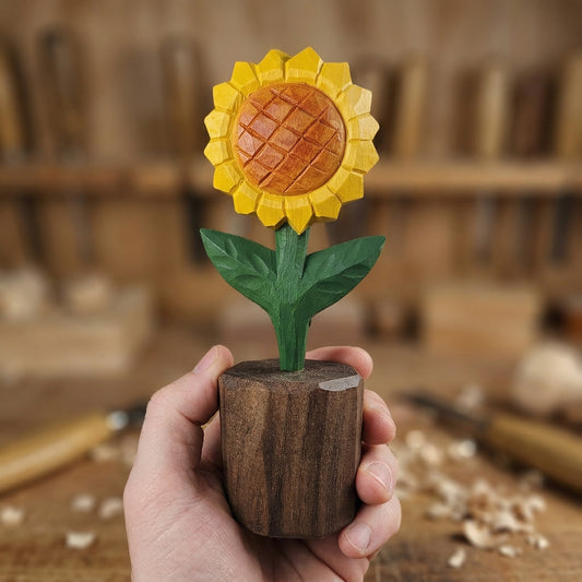 Hand holding a wooden sunflower figurine in a workshop setting