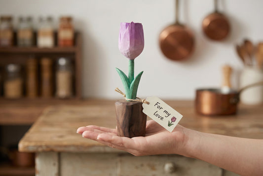 Person holding a small purple tulip plant with a tag in a kitchen setting
