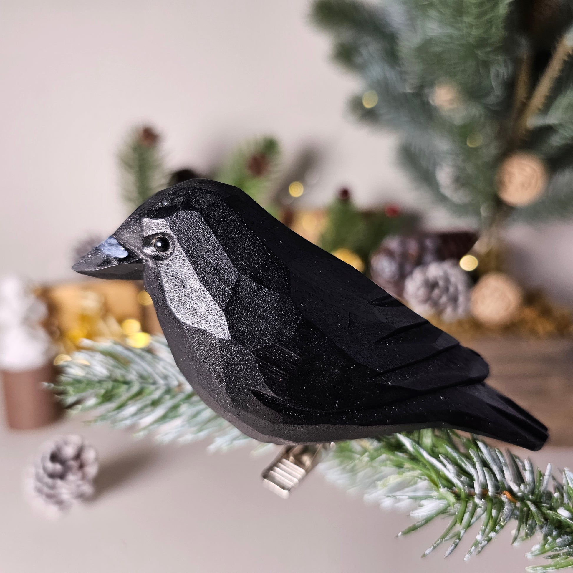 Hand-carved solid basswood American Crow clip-on ornament perched on a pine branch, showing glossy black hand-painted plumage detail