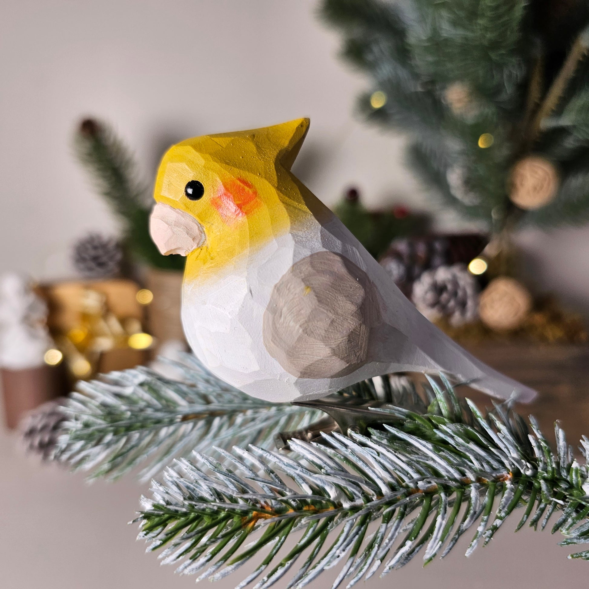 Hand-carved solid basswood Cockatiel clip-on ornament in Gray, showing yellow crest, orange cheek patches, and long tapered tail — by Painted Bird Shop.