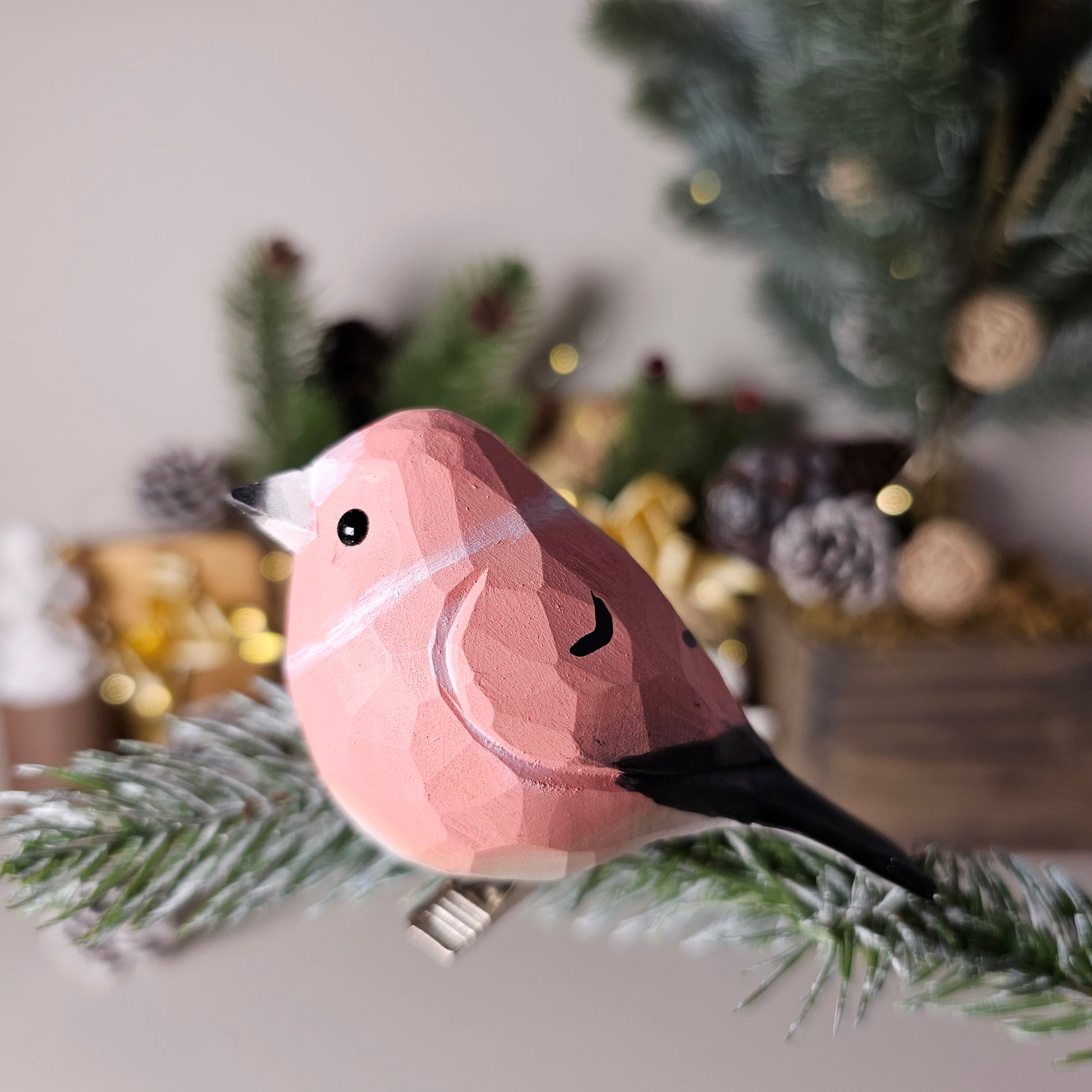 Hand-carved solid basswood Common Rosefinch clip-on bird ornament, showing vivid crimson-red head and breast with warm brown upperparts, clipped to a pine branch
