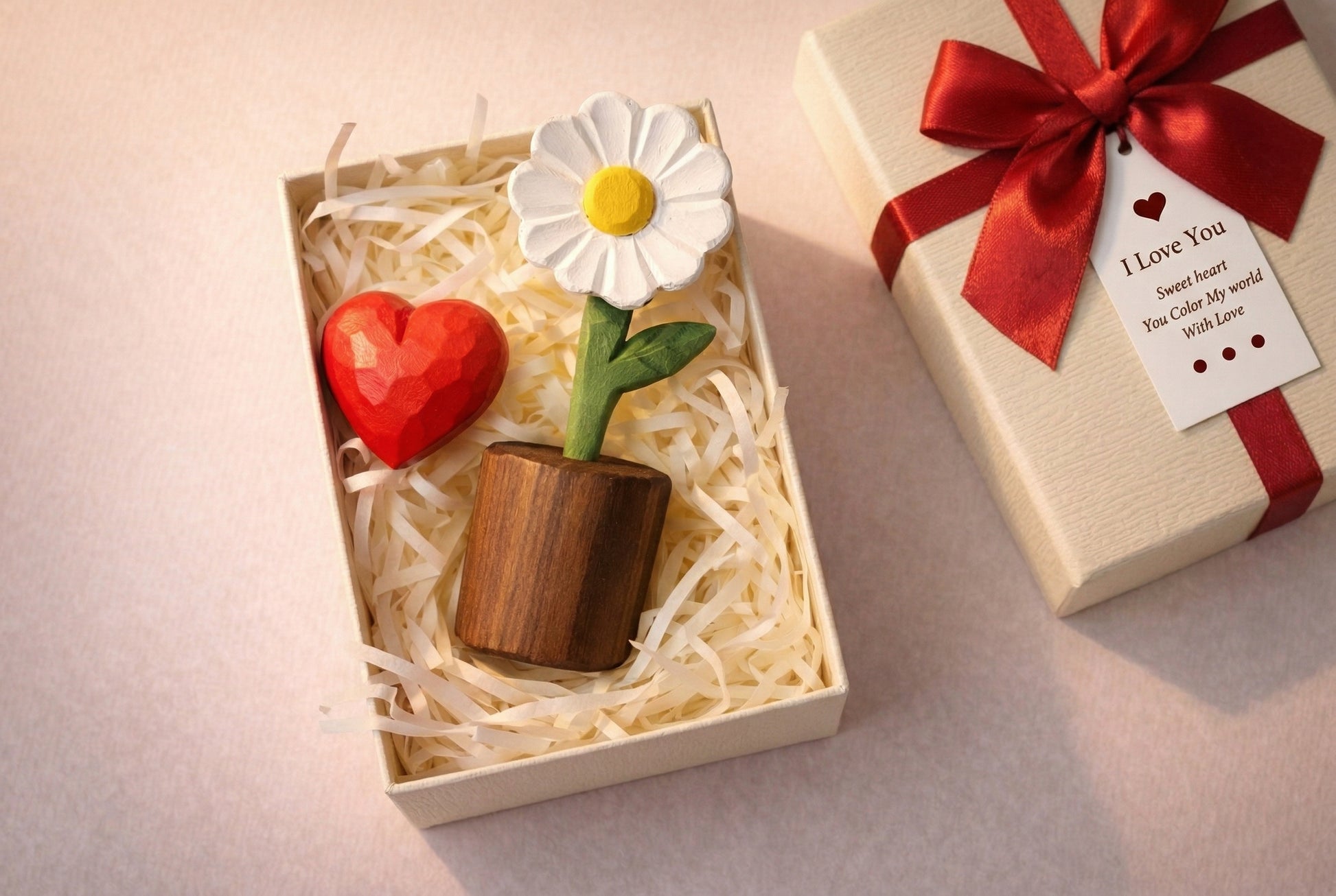 Decorative items including a heart, flower, and small pot in a box, with a gift box and 'I Love You' tag in the background.