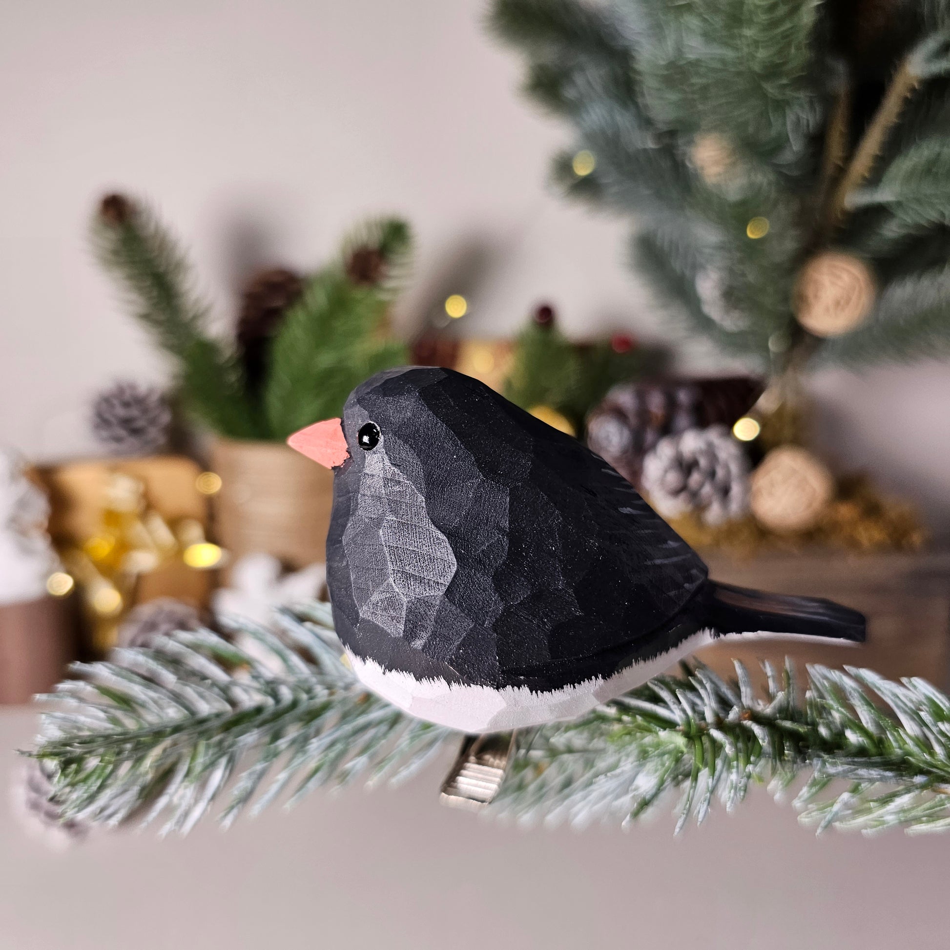Hand-carved solid basswood Dark-eyed Junco clip-on bird ornament, showing slate-grey hood and white tail feathers, clipped to a pine branch