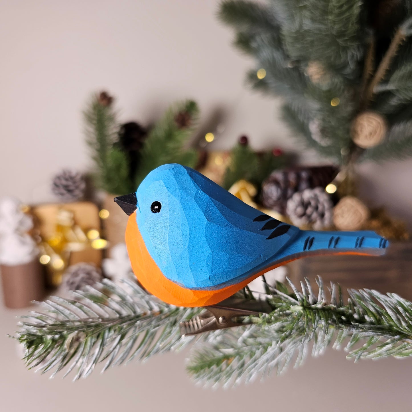 Hand-carved solid basswood Eastern Bluebird clip-on ornament perched on a pine branch, showing vivid cobalt-blue wings and russet breast hand-painted detail