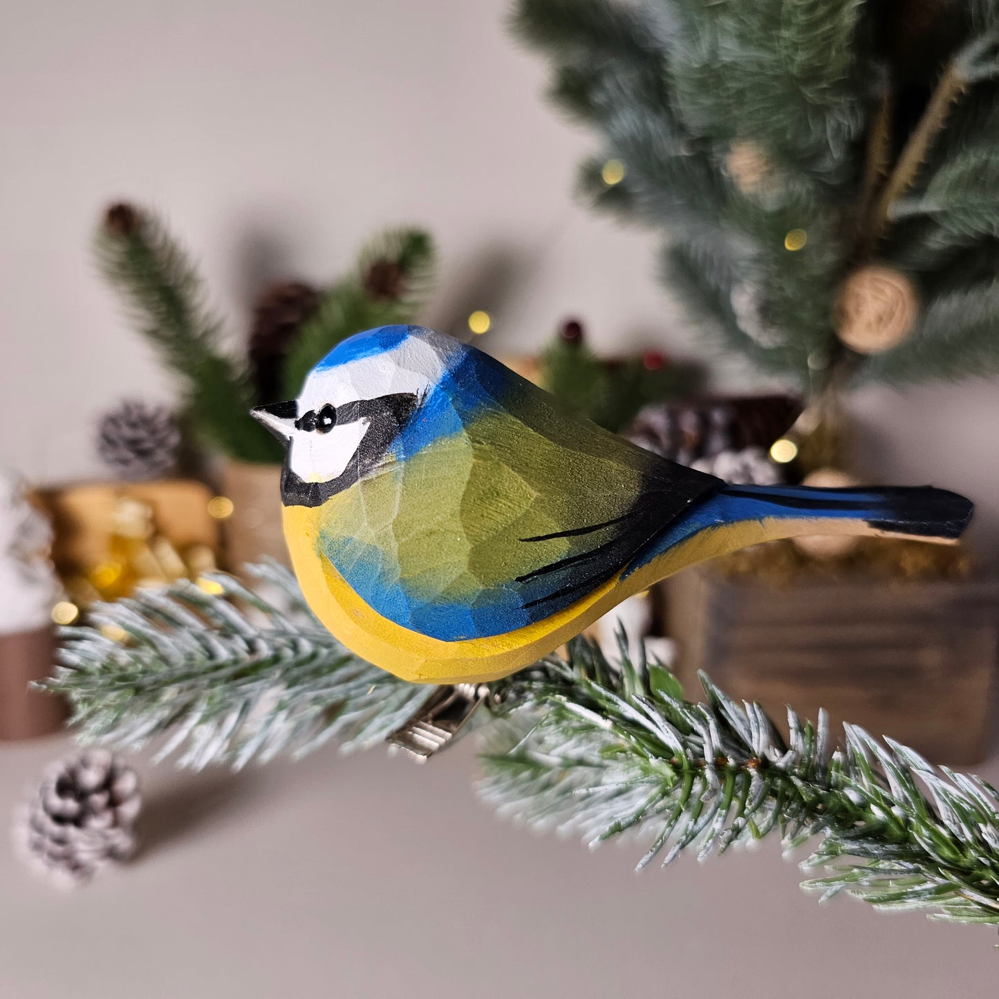 Hand-carved solid basswood Eurasian Blue Tit clip-on ornament perched on a pine branch, showing vivid cobalt-blue cap and yellow belly hand-painted detail