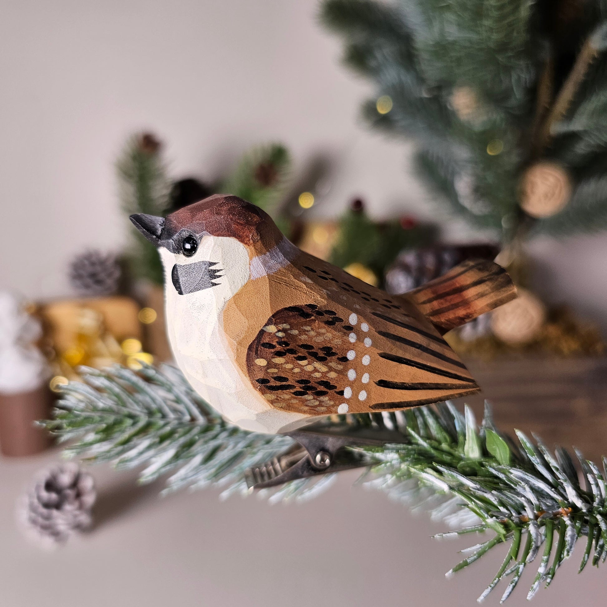 Hand-carved solid basswood Eurasian Tree Sparrow clip-on bird ornament, showing chestnut crown, white cheeks and black ear patch, clipped to a pine branch