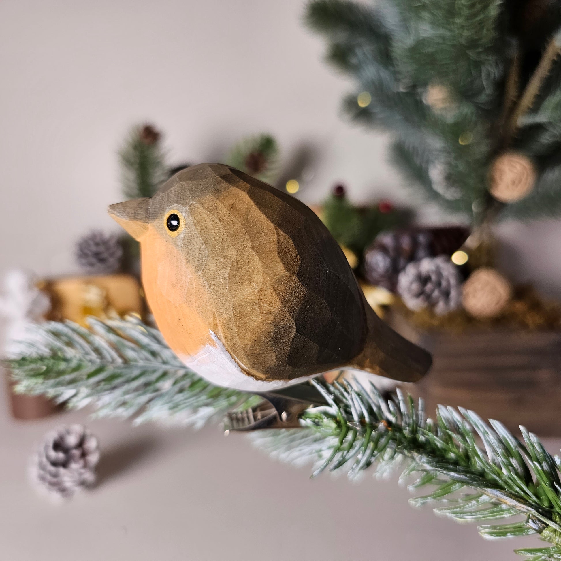 Hand-carved solid basswood European Robin clip-on ornament perched on a pine branch, showing flame-orange breast and hand-painted brown plumage detail