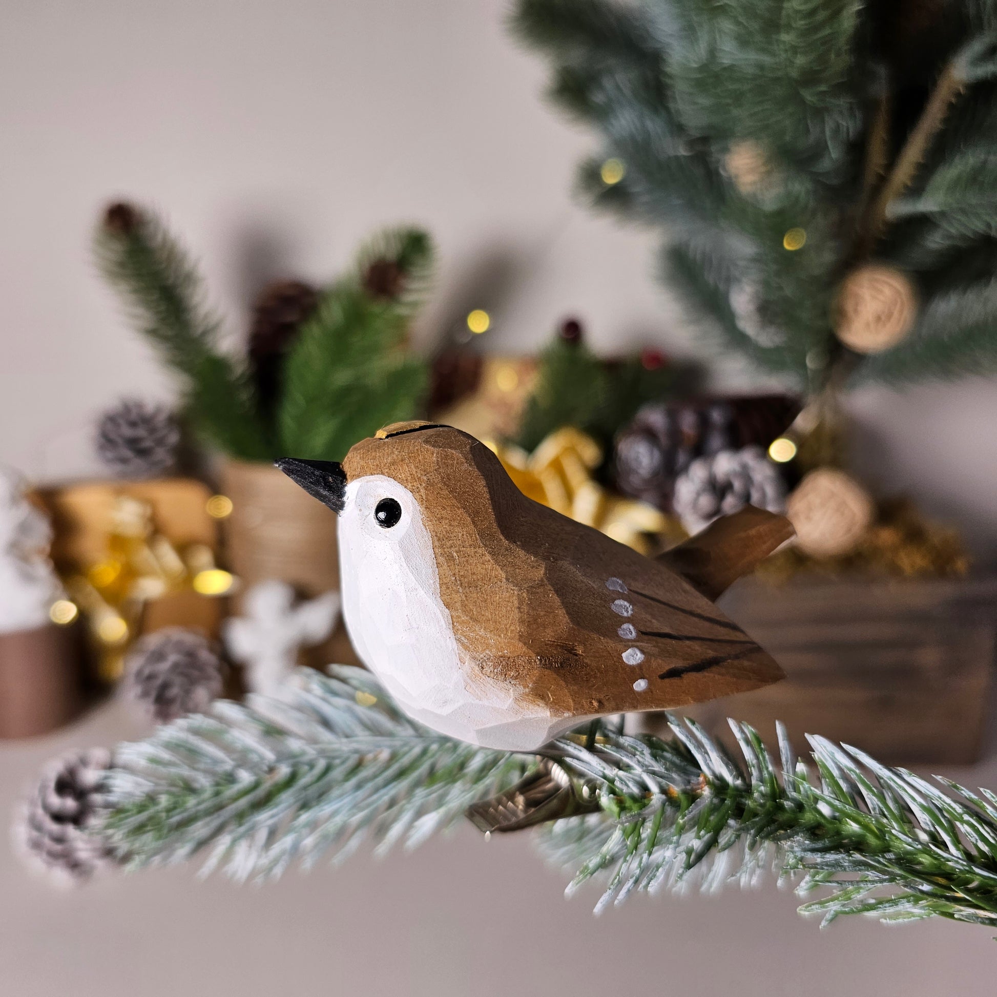 Hand-carved solid basswood Goldcrest clip-on ornament perched on a pine branch, showing golden crown stripe and olive-green hand-painted plumage detail