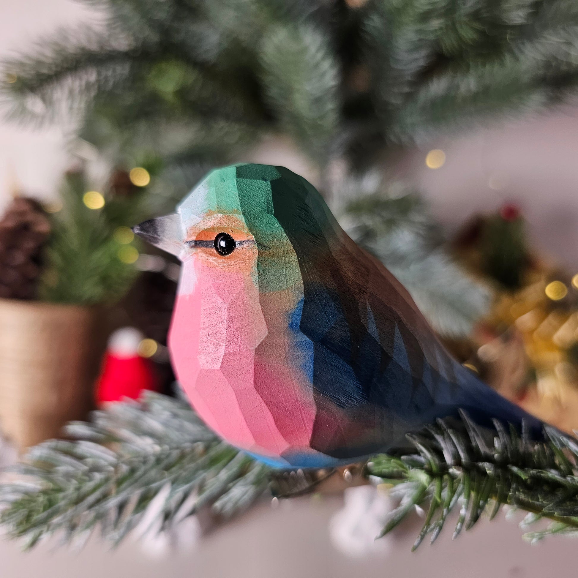 Hand-carved solid basswood Lilac-breasted Roller clip-on bird ornament, showing vivid turquoise, lilac, and chestnut plumage, clipped to a pine branch