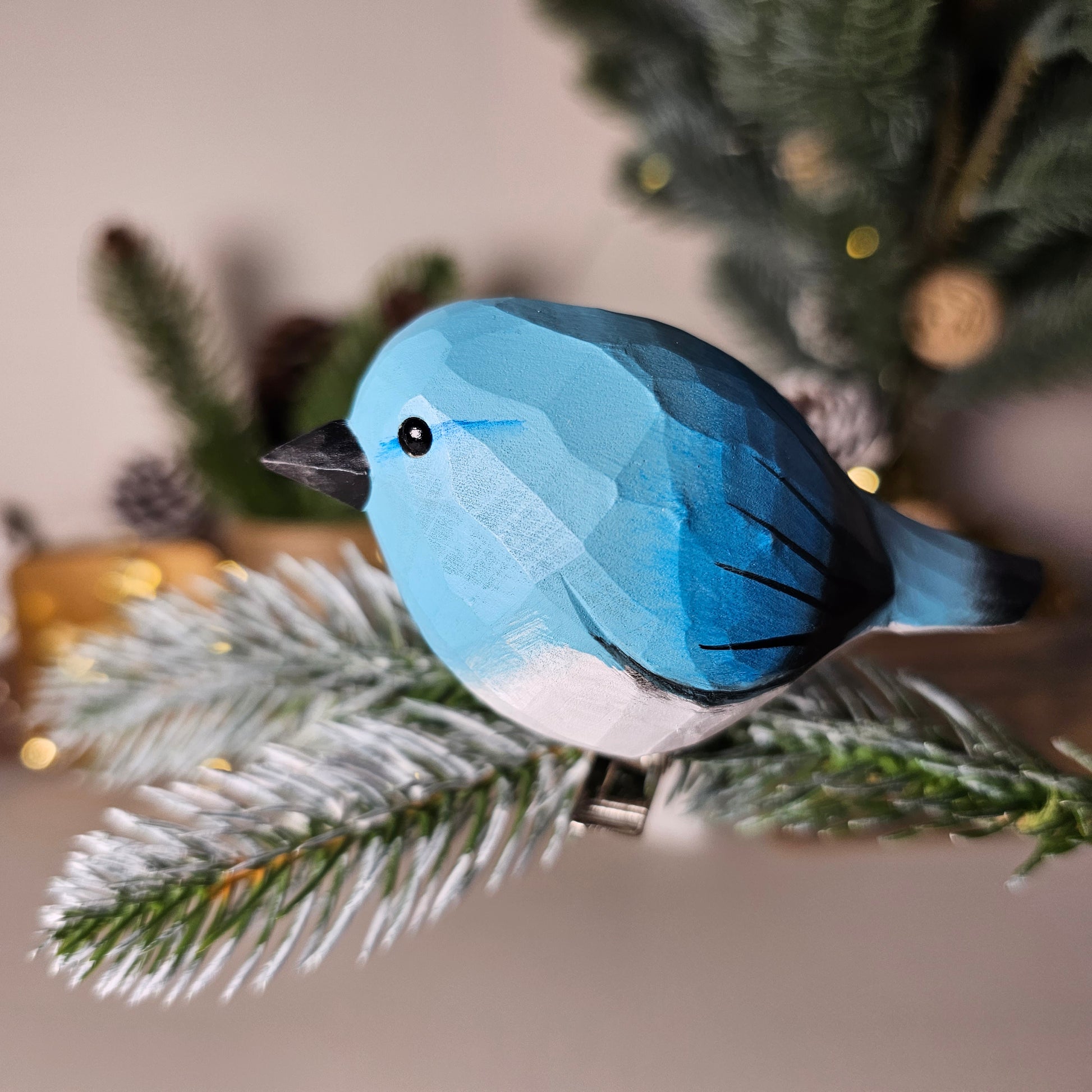 Hand-carved solid basswood Mountain Bluebird clip-on ornament showing luminous all-sky-blue plumage, pale underparts, and slender thrush silhouette — by Painted Bird Shop.