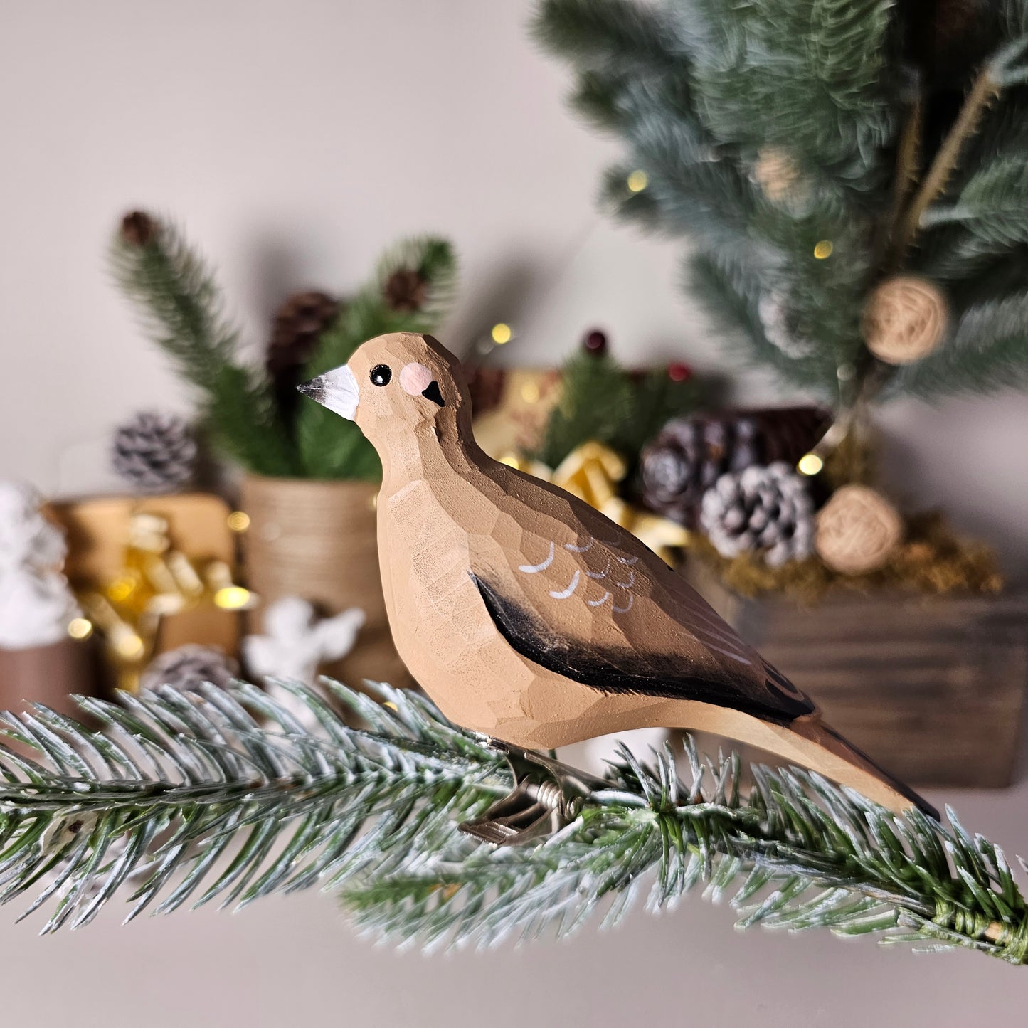 Hand-carved solid basswood Mourning Dove clip-on bird ornament, showing soft grey and buff plumage with tapered tail, clipped to a pine branch