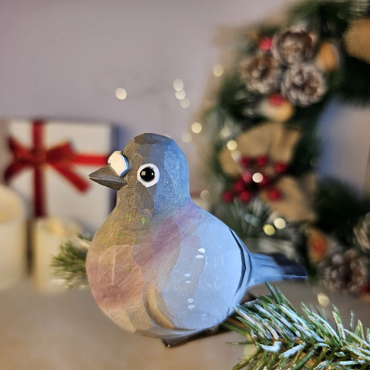 Hand-carved solid basswood Rock Pigeon clip-on ornament in gray, showing detailed wing barring and iridescent neck painting, displayed on a pine branch