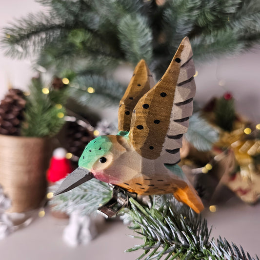 Hand-carved solid basswood Ruby-throated Hummingbird clip-on ornament with hand-painted green and red plumage, shown clipped to a pine branch
