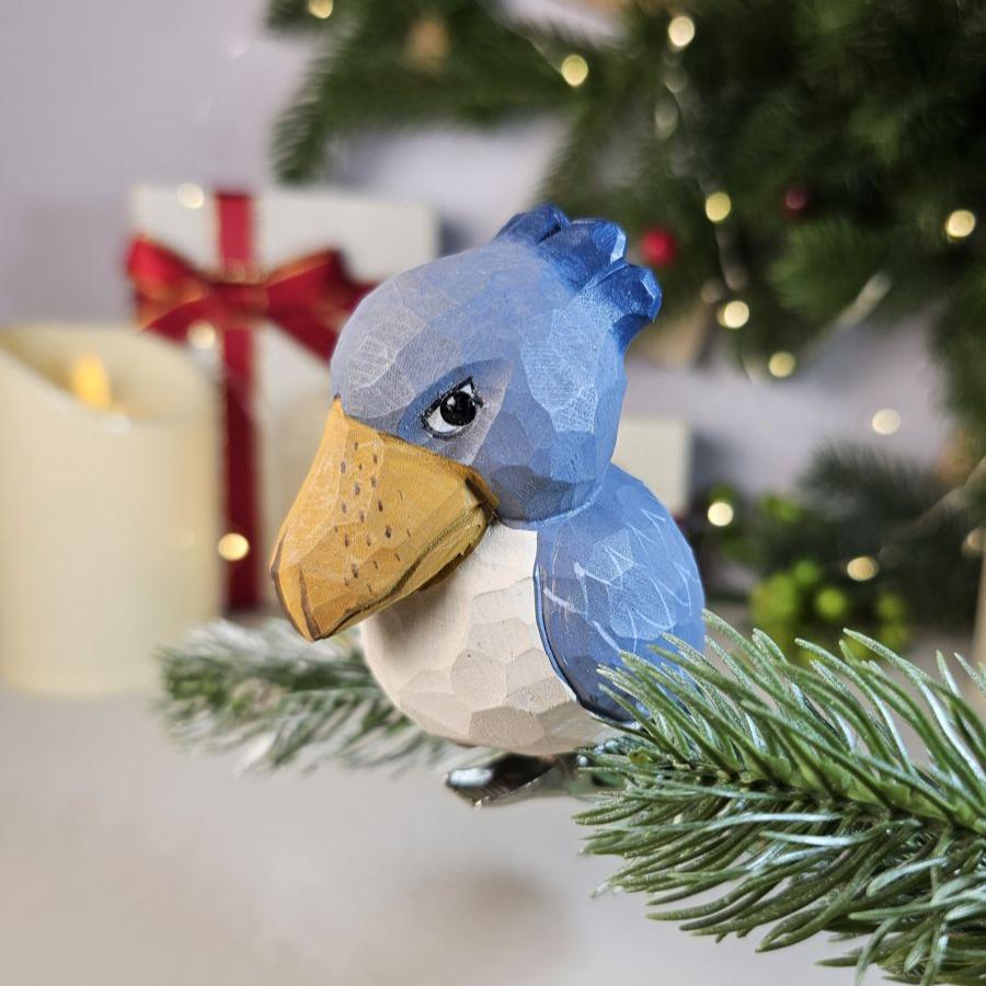 Hand-carved solid basswood Shoebill clip-on bird ornament with slate-blue plumage and distinctive hook-tipped bill, displayed on a pine branch