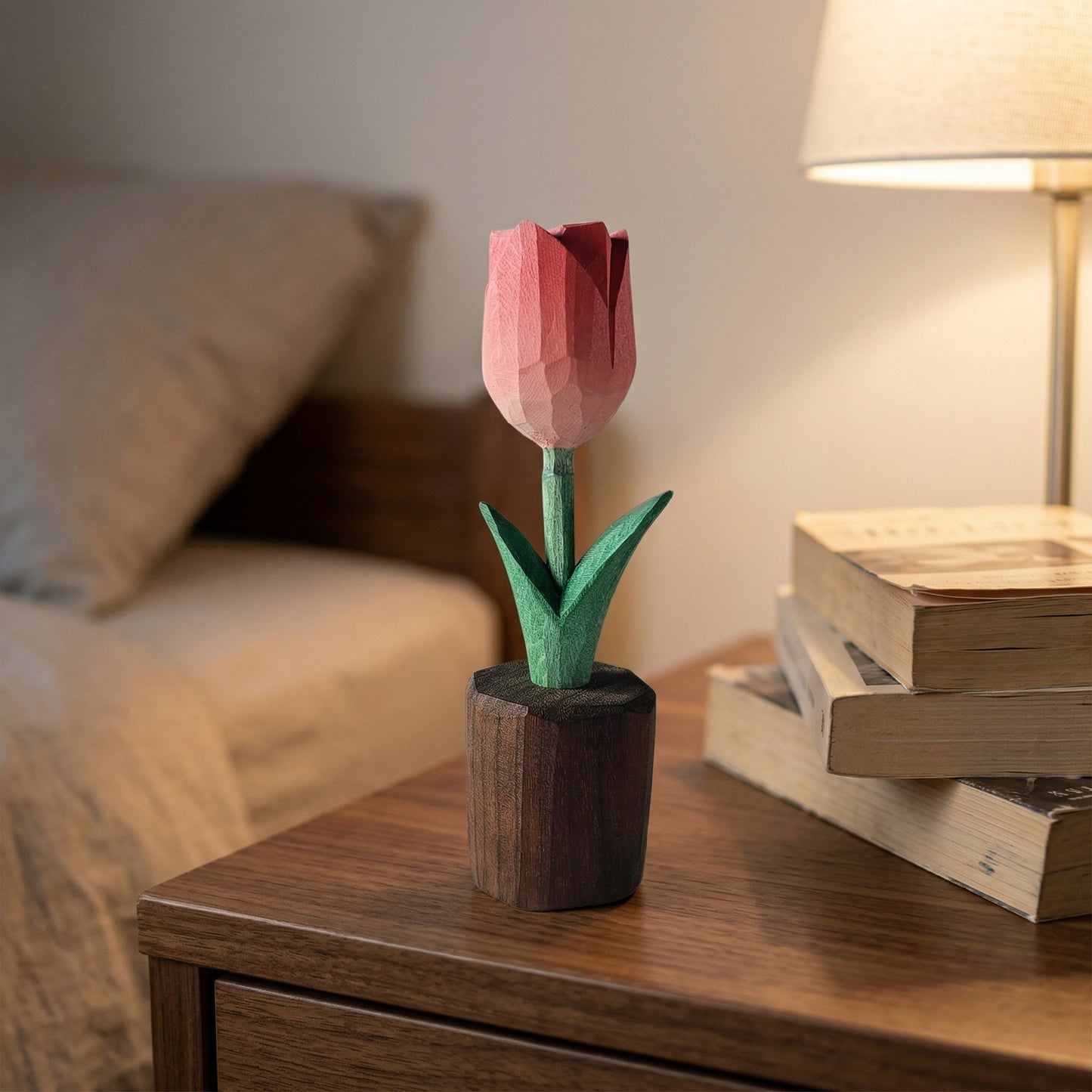 Pink tulip-shaped object on a wooden surface with books and a lamp in the background