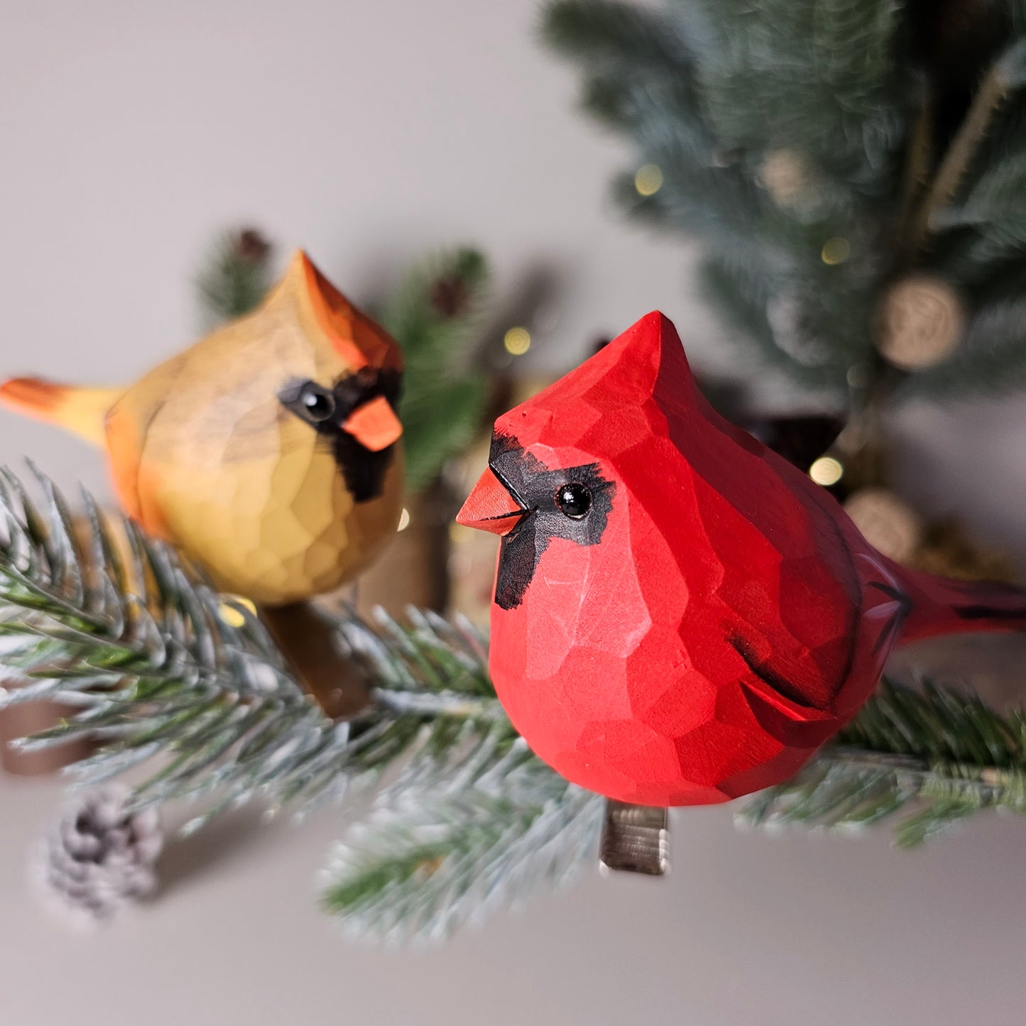 Hand-carved wooden Northern Cardinal clip-on ornaments in red and gold, displayed on a holiday pine branch.