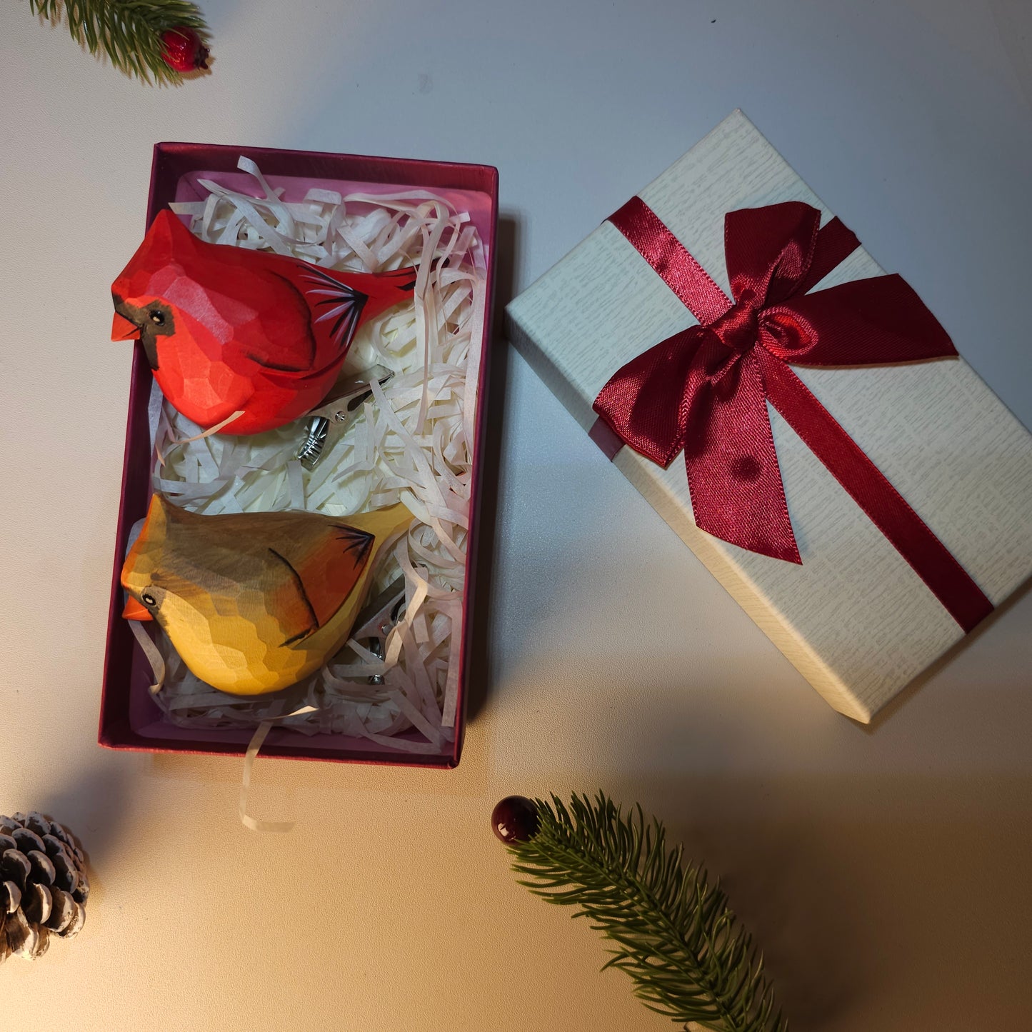 Hand-carved wooden Northern Cardinal ornaments in red and gold displayed in a holiday gift box with a red ribbon.