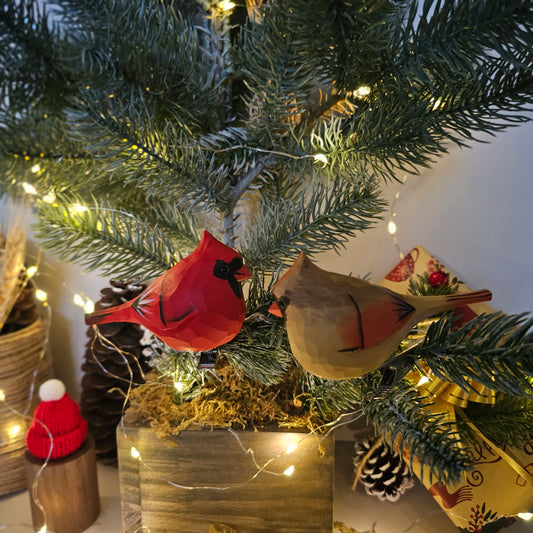 Pair of hand-carved wooden Northern Cardinal clip-on ornaments resting on a pine branch with warm holiday fairy lights