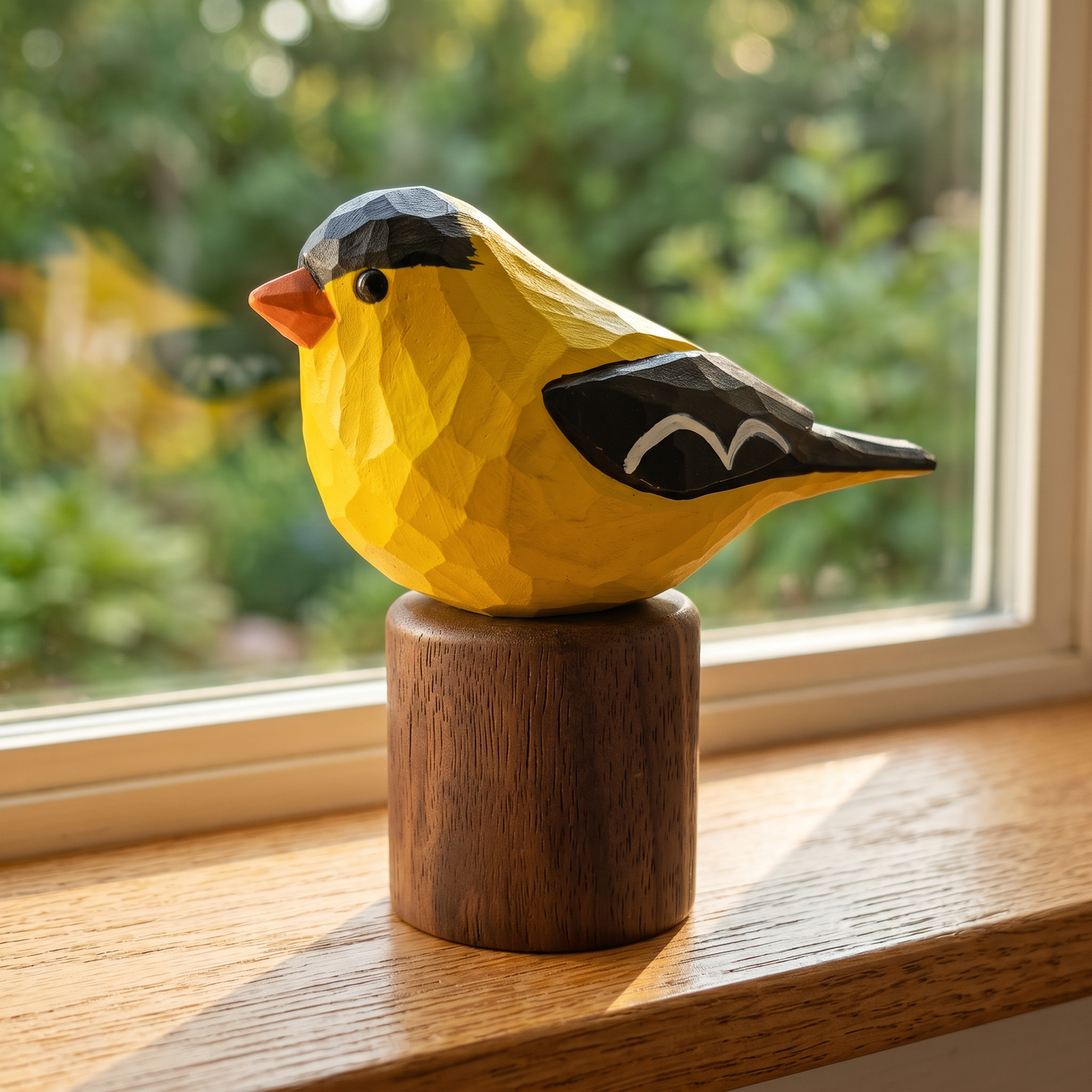Hand-painted American Goldfinch wooden figurine on a walnut base, displayed on a sunny windowsill with garden greenery